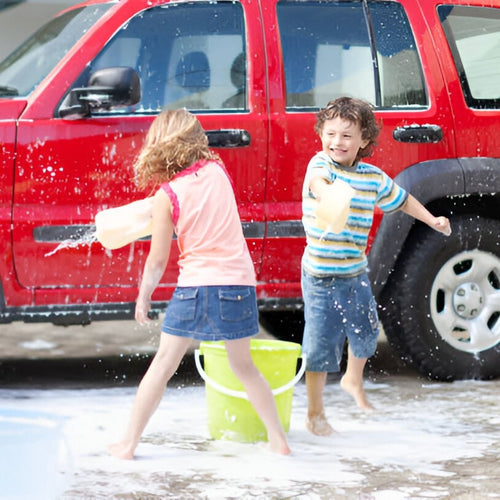 Two kids playing in water while washing red SUV