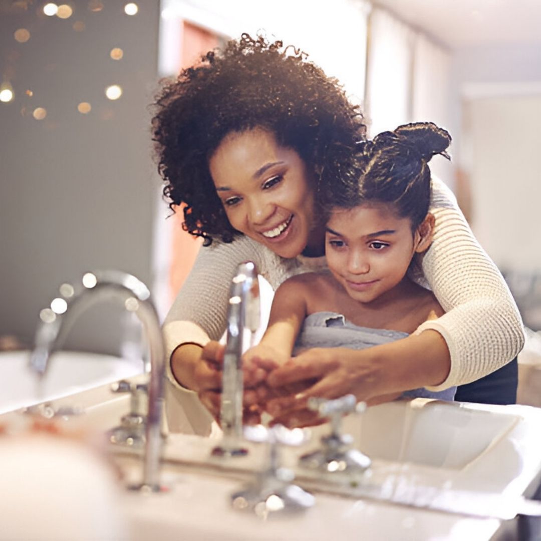 African American mom with daughter washing hands in bathroom