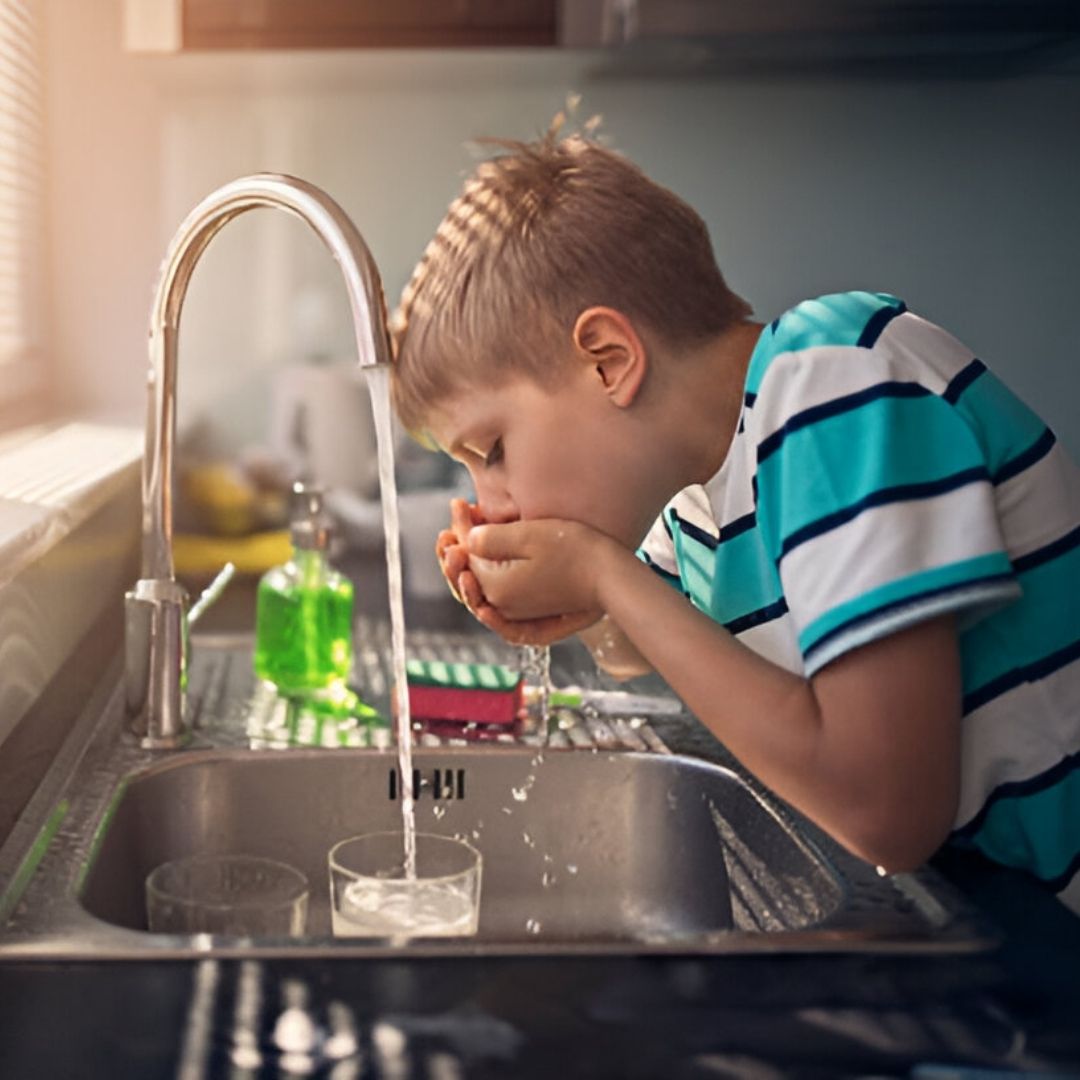 Boy drinking water from hands at kitchen sink