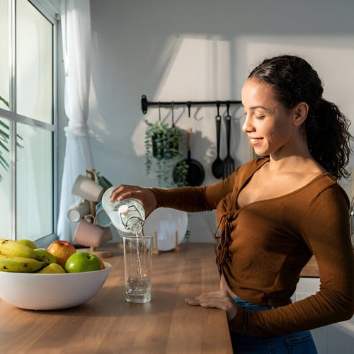Latina woman smiling pouting water into glass on kitchen countertop