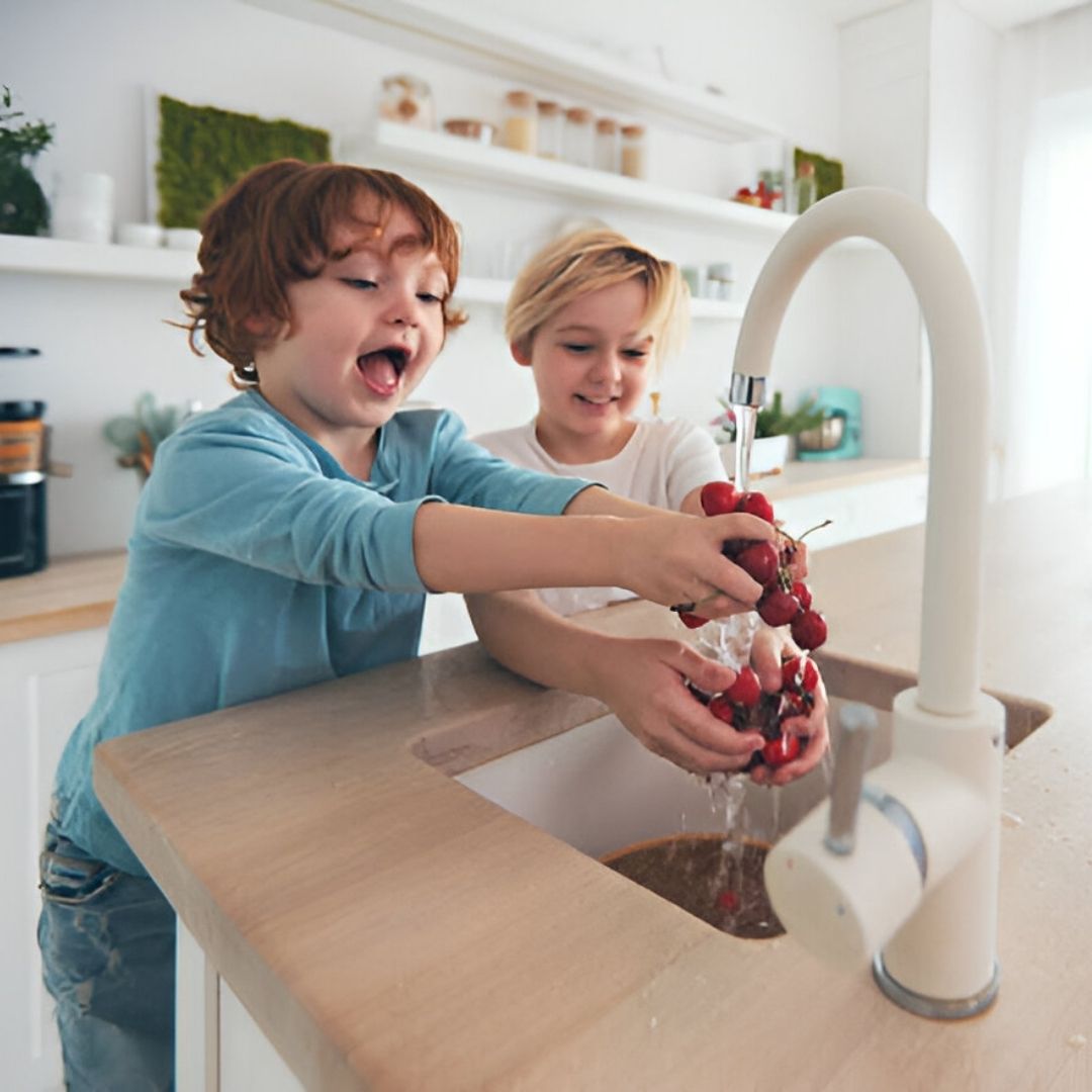 Two young girls washing cherries in kitchen sink